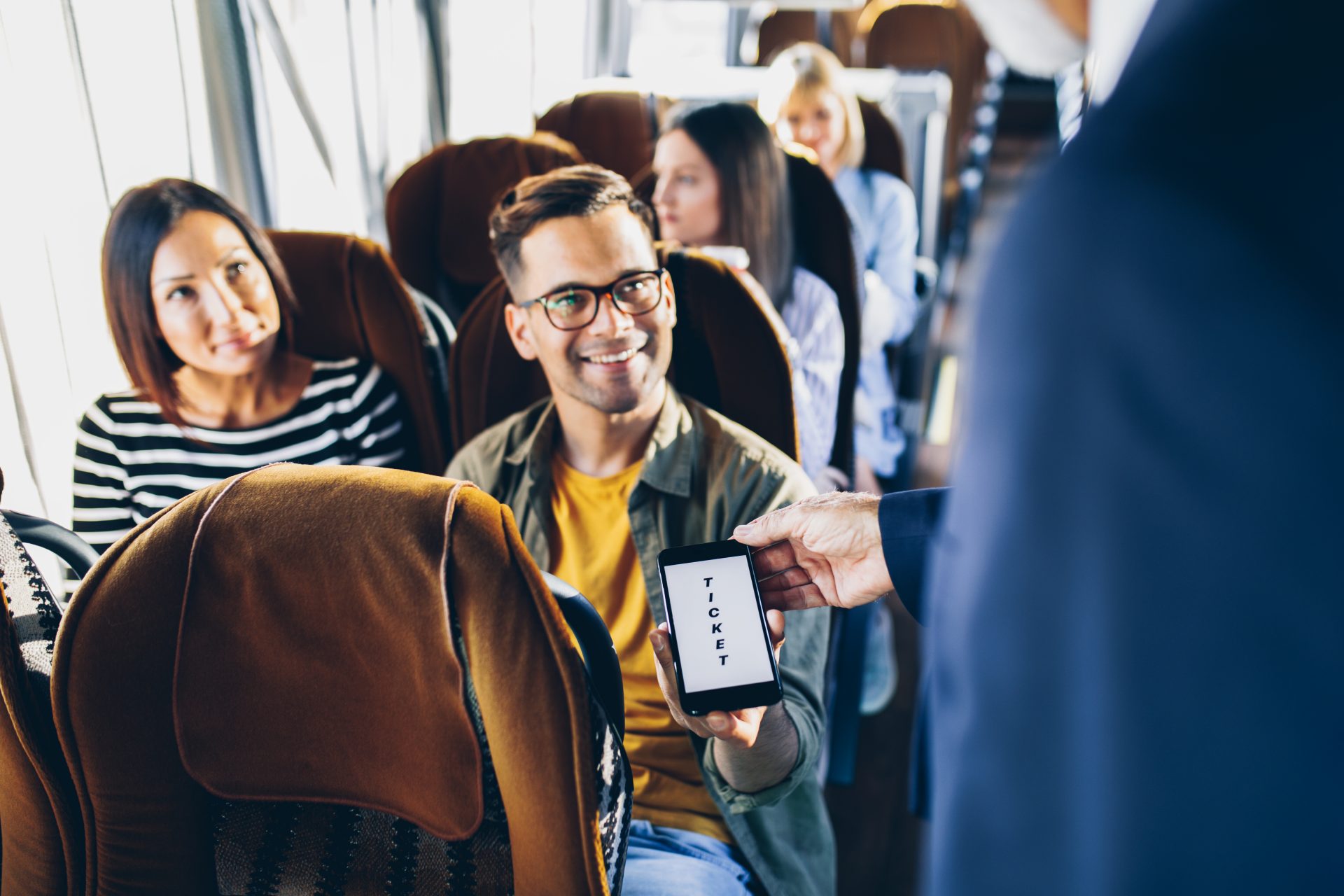 Young male traveler showing e-ticket on mobile phone screen to a bus driver.