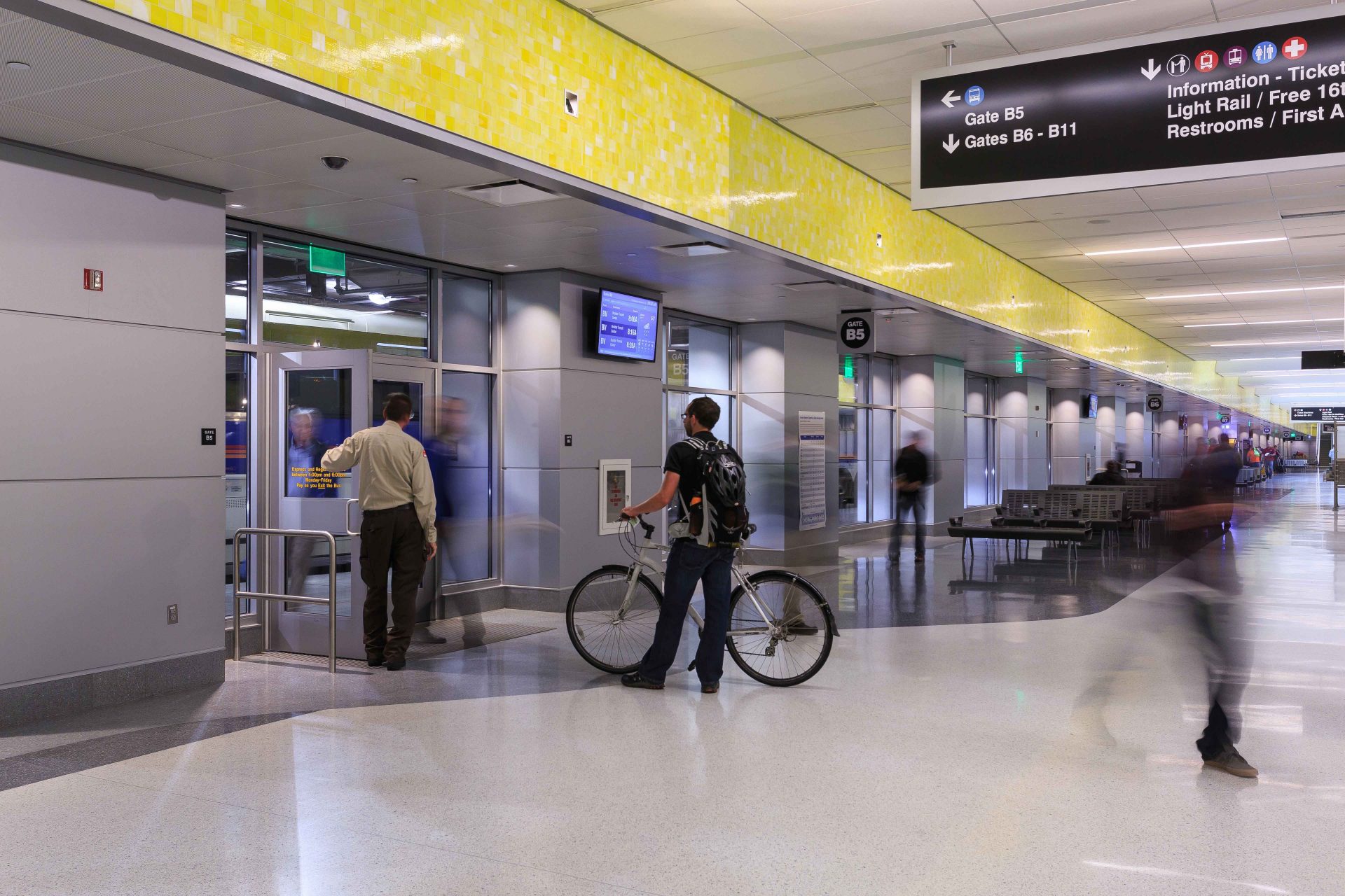 People mill about an indoor bus terminal, a man holds a door open letting people through.