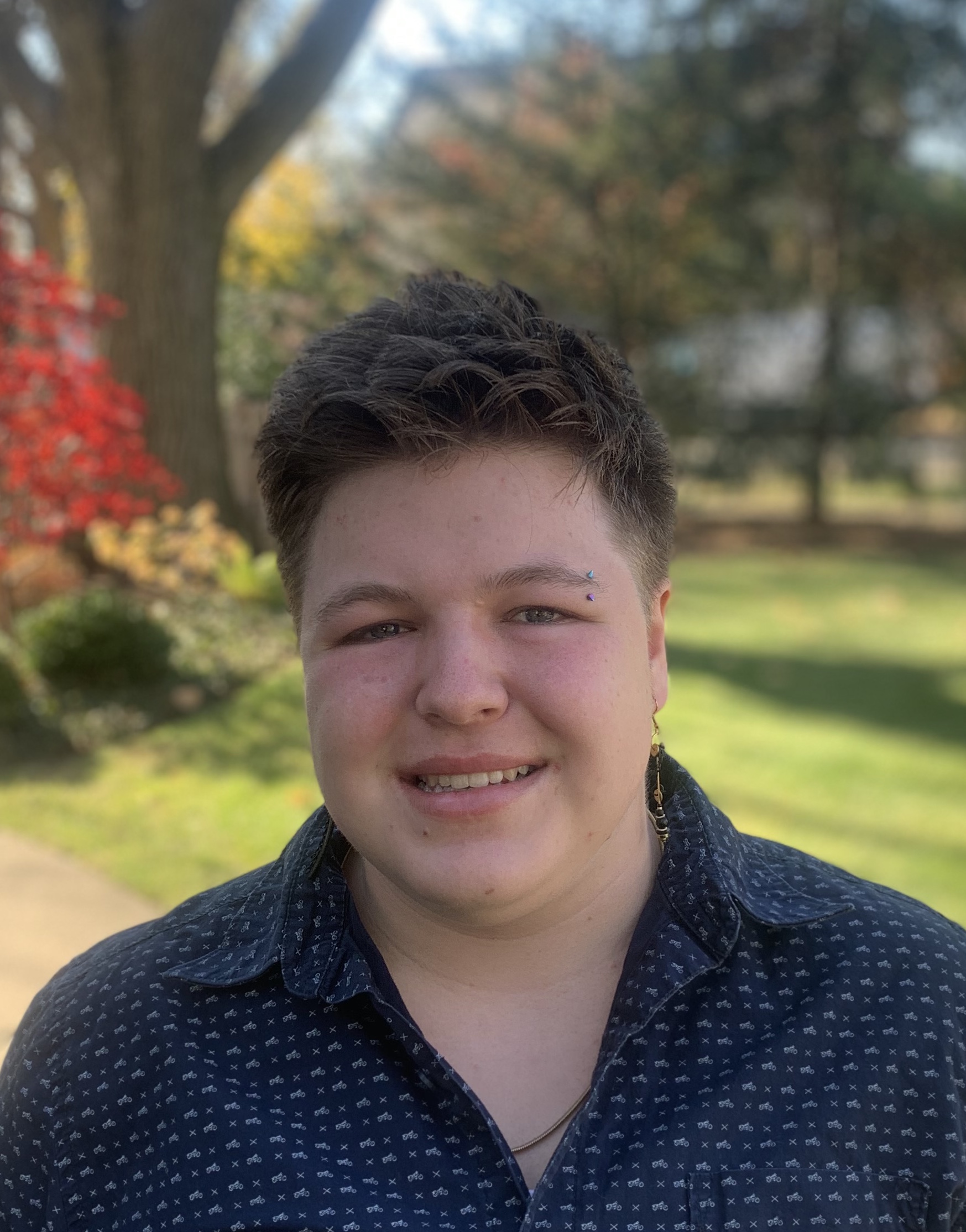 A photo of Sage Kashner from the shoulders up, smiling and wearing a collared shirt.
